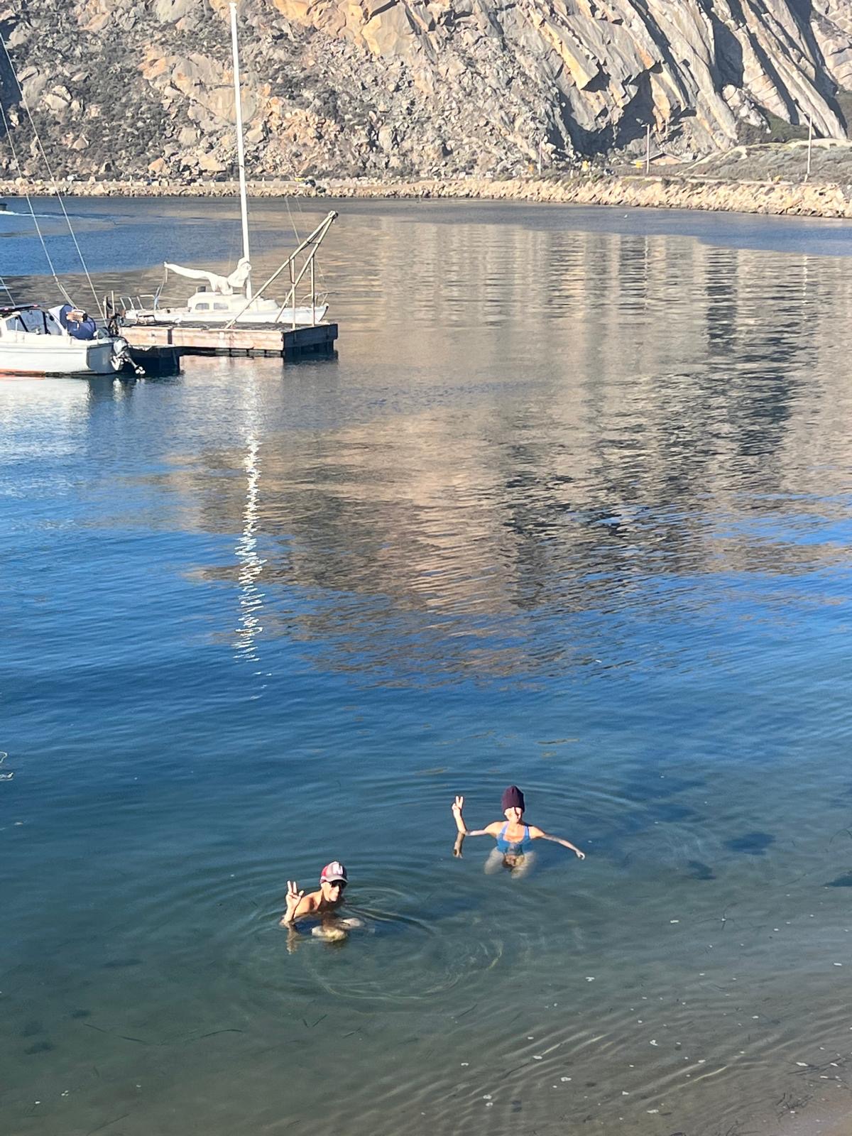 Two odders throwing peace signs in deep blue water below the rock face